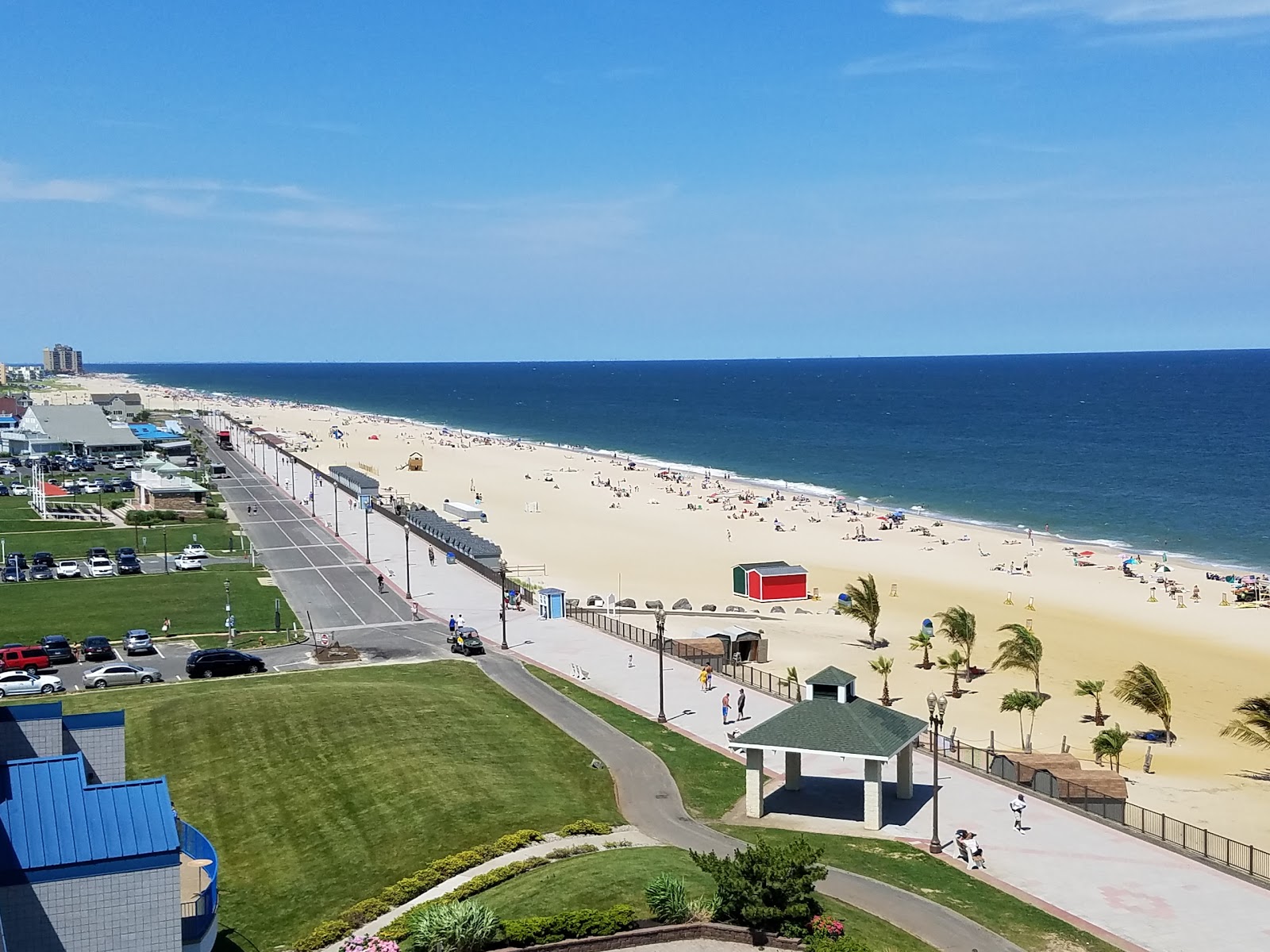 Aerial view of Long Branch beachfront in NJ, with a wide sandy shoreline, boardwalk promenade, and calm ocean waters under a clear blue sky