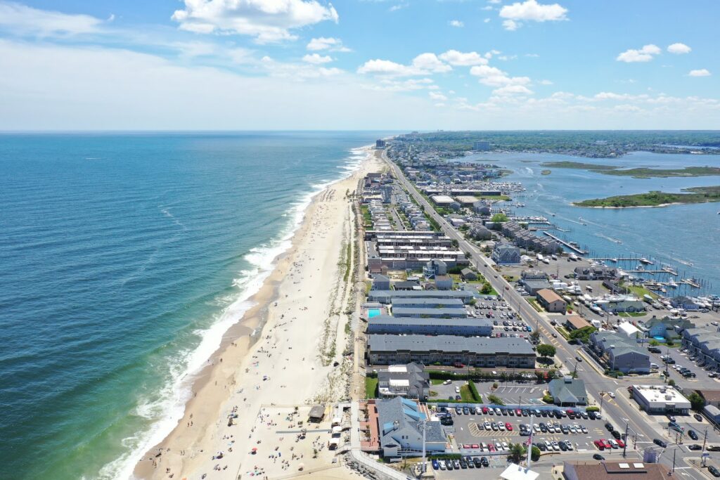 A webpage slide titled 'Oceanfront vs. Riverfront Living' comparing properties, featuring bullet points of economic and real estate benefits and an aerial photo of a coastal town flanked by the Atlantic Ocean and a river with marinas.