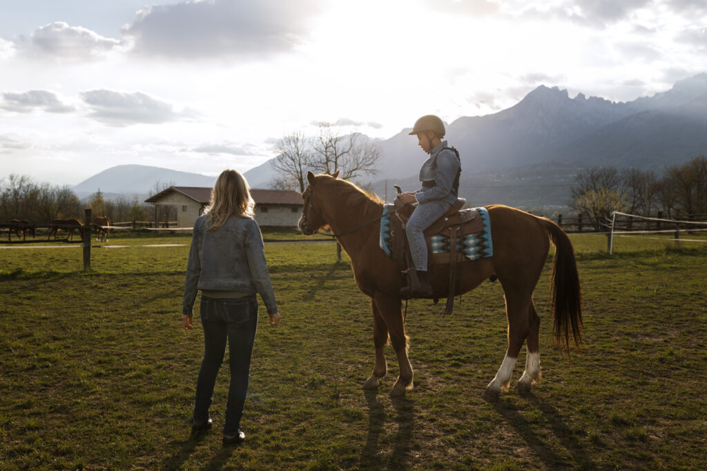 Woman standing in a green pasture talking to a person horseback riding