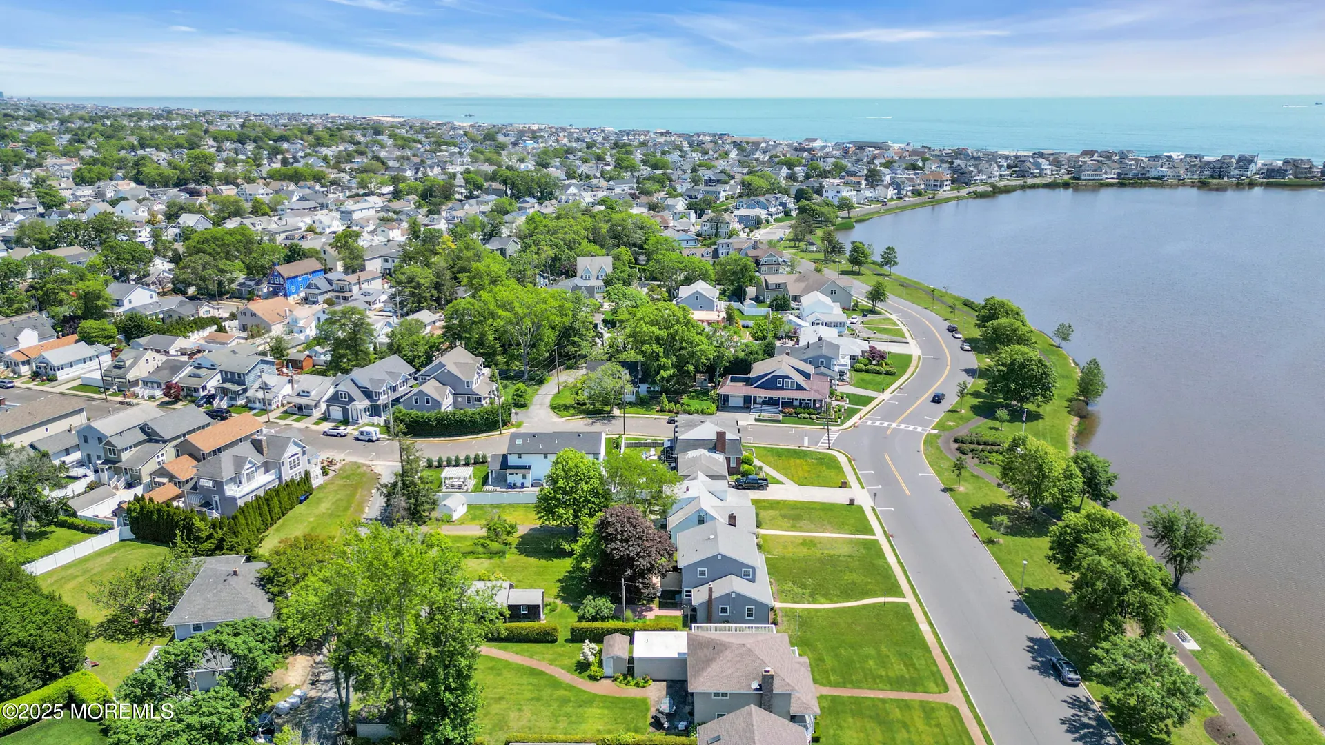 Aerial view of Lake Como, NJ, with a quiet residential neighborhood of tree-lined streets and well-kept homes bordering a calm lake, with the Atlantic Ocean visible in the distance