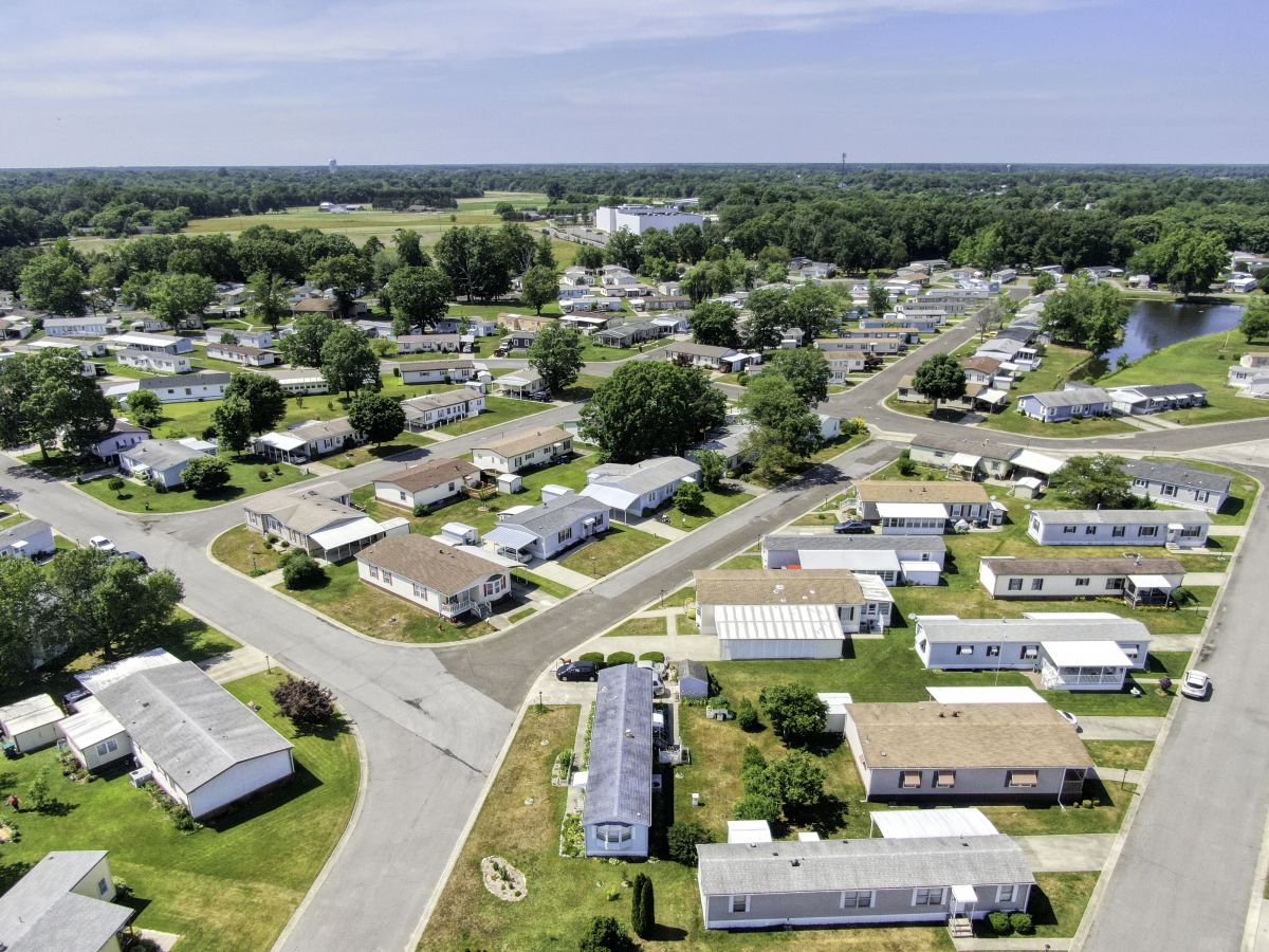 Aerial drone view of a residential active adult community in Manahawkin, NJ, with rows of single-story homes, tree-lined streets, and a small pond surrounded by lush greenery