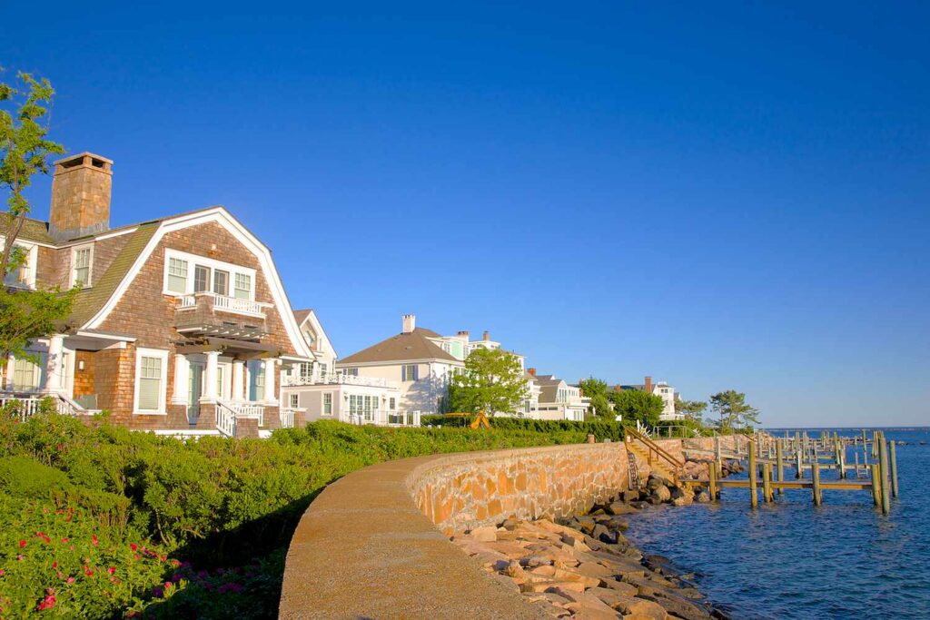 Coastal home with a stone sea wall, green landscaping, and a wooden dock on a sunny day