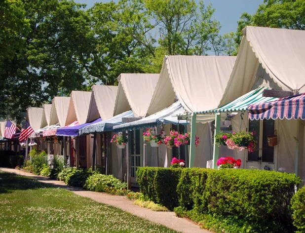 Row of charming historic tent cottages with colorful awnings and flower boxes along a tree-lined path in Ocean Grove, NJ