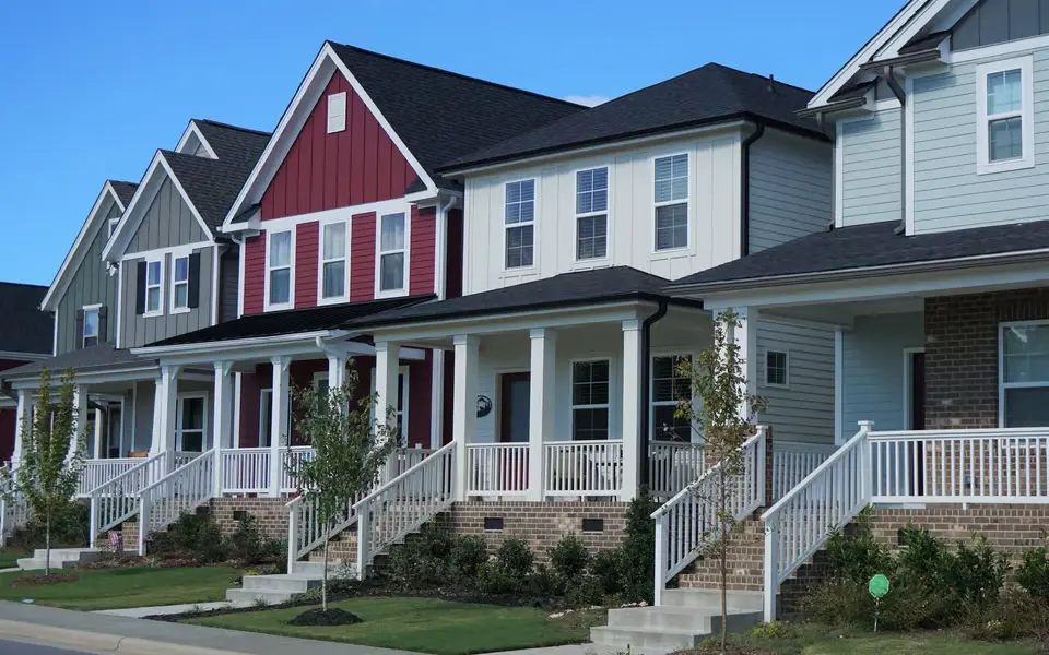 A row of colorful, modern two-story suburban houses with white porches and railings under a clear blue sky in Howell Township.