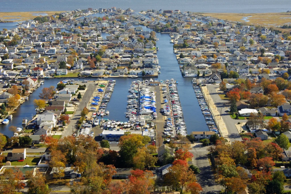 Aerial view of Brick Township, NJ in fall foliage, with dense residential neighborhoods, a large marina packed with boats, and waterways extending toward Barnegat Bay