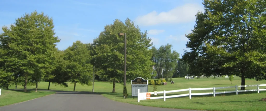 Scenic tree-lined entrance to a rural property in Allentown, NJ, with a classic white split-rail fence, manicured lawn, and lush mature trees typical of Monmouth County's equestrian corridor