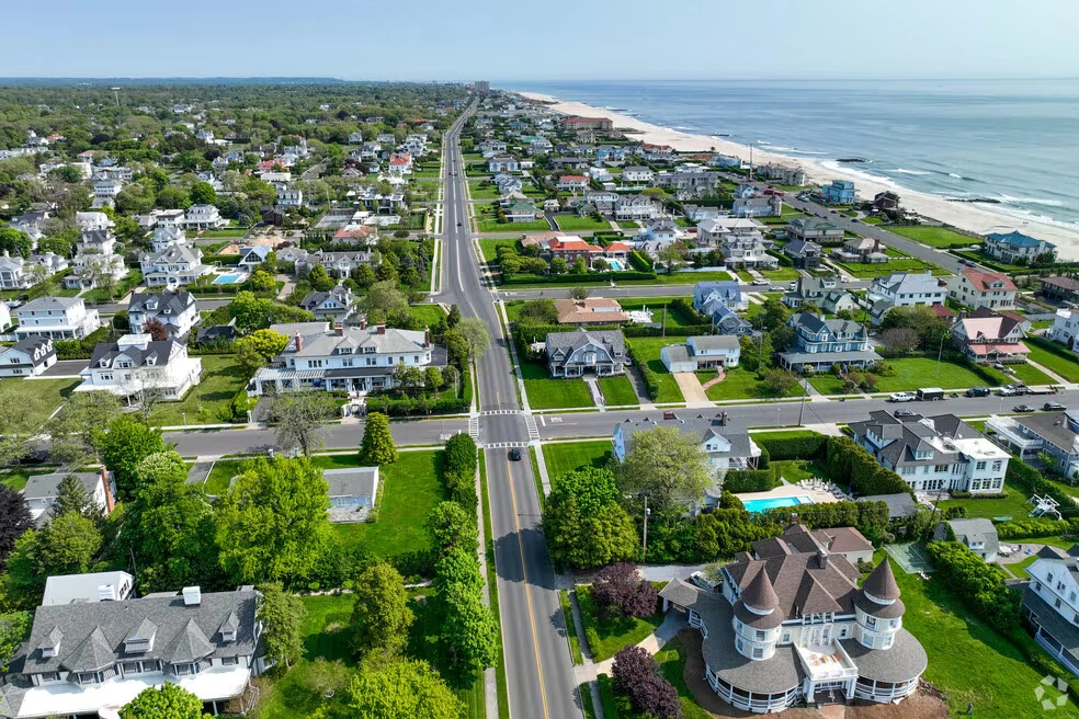 Aerial view of Deal, NJ, with tree-lined streets, expansive upscale homes with lush green lawns, and the Atlantic Ocean shoreline stretching along the coast on a clear spring day