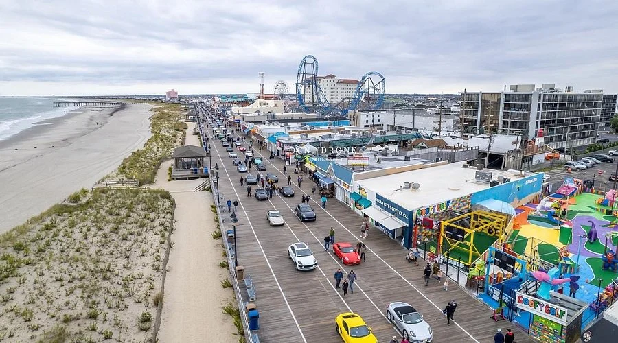 Aerial view of the Ocean County boardwalk in NJ, with the Atlantic Ocean shoreline, sandy dunes, busy shops, and amusement rides stretching along the coast